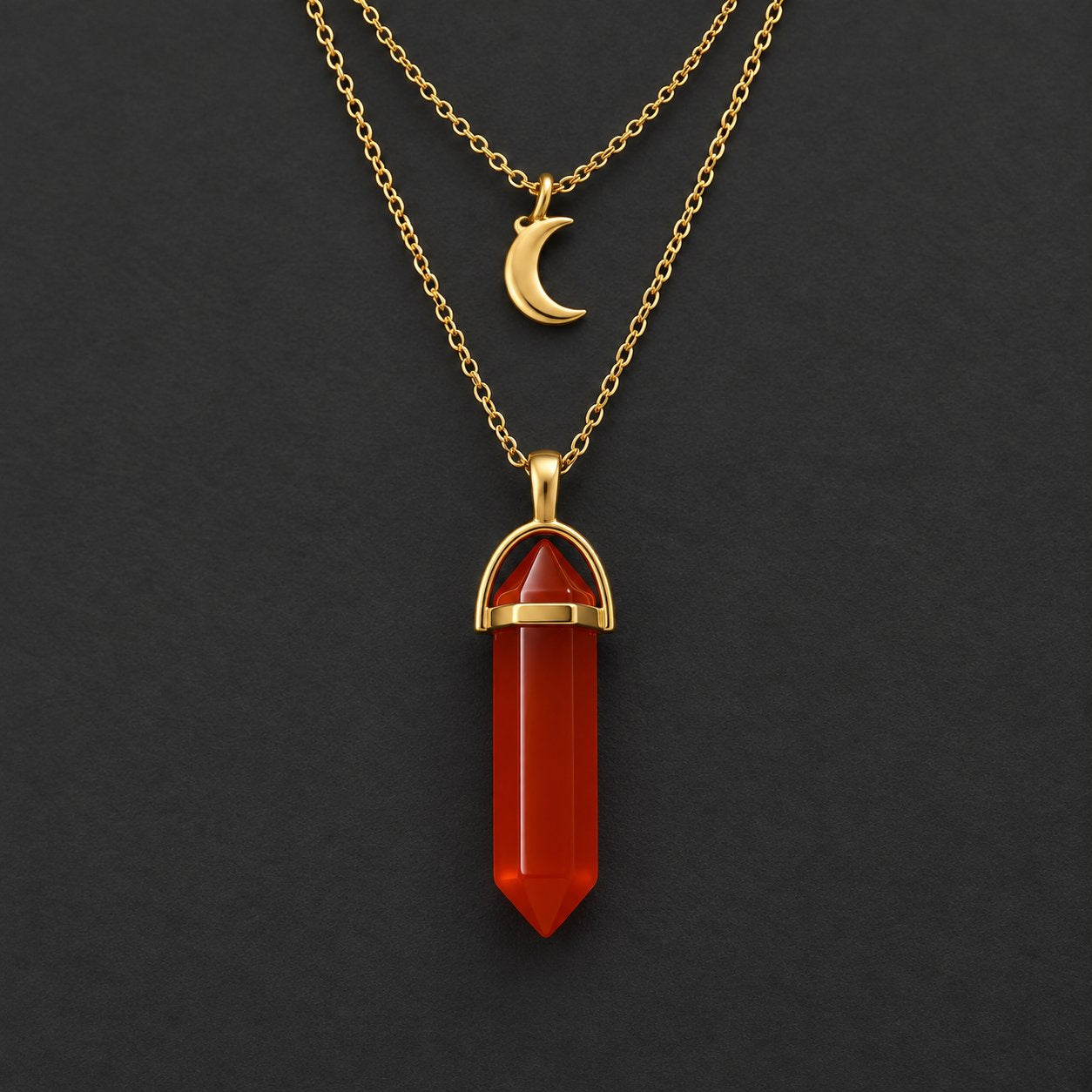 The Pomence Carnelian Attraction Necklace laid out on a dark ground showing both chains and the carnelian point