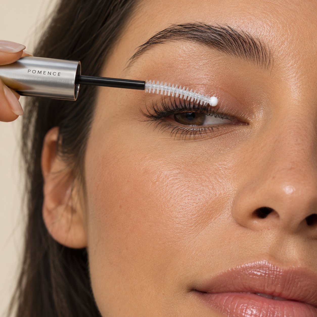 A woman combing the curved spooly brush of the Pomence serum wand through her upper lashes