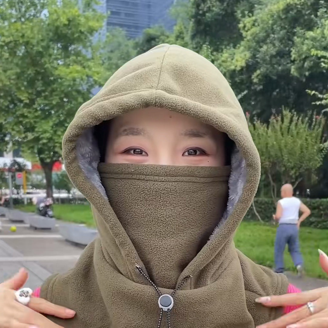 A young woman outdoors in the green hood, the face cover up to her eyes, the round cord lock at her collar.