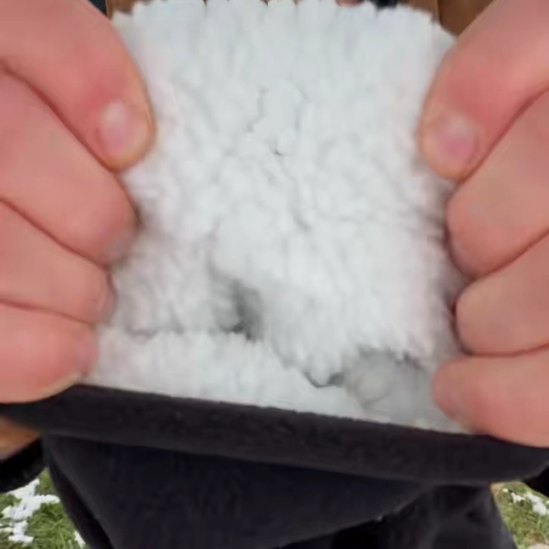 Two hands stretch open the thick white plush lining of a black hood at a snowy farm stall, the cord lock below.
