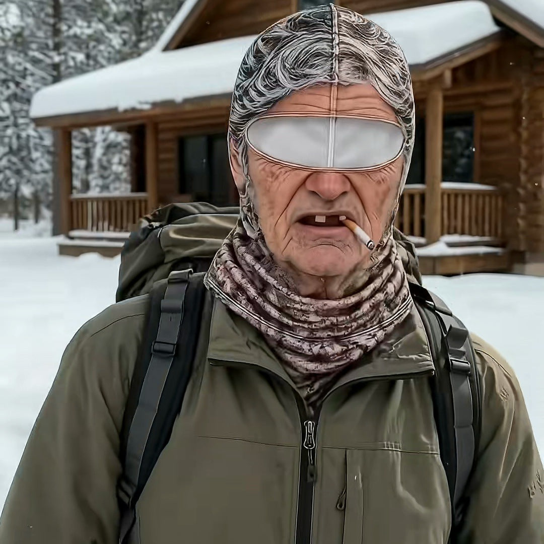 A man in an olive jacket and backpack wearing the Grandma mask in front of a snowy log cabin.
