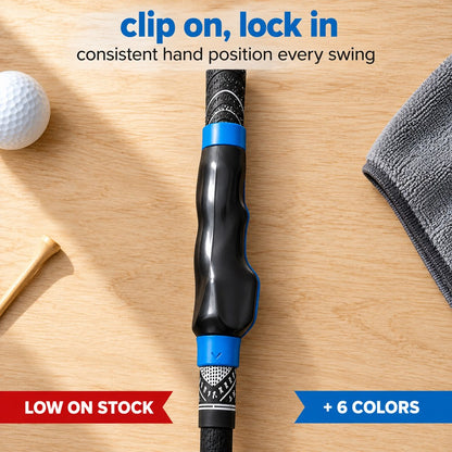 Pomence Golf Grip Trainer, a black clip-on shell with blue collars snapped over a golf club grip, shown flat with a ball and a tee