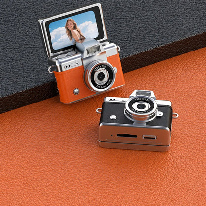 Two Pomence Mini Keychain Cameras in orange and black on a leather surface