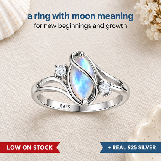 Flat lay of the Pomence Moonstone Ring on pale linen, the marquise moonstone flashing blue between two crossing silver ribbons