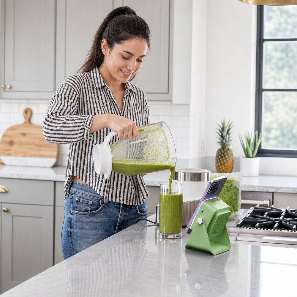 The green Pomence Speaker Phone Stand holding a phone on a kitchen counter while a woman pours a smoothie