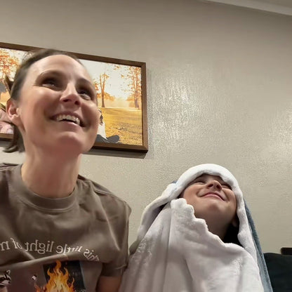 a mom smiling on the couch beside her son, who sits in the shark hood just after opening it
