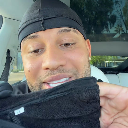 A man in a black durag in his car holding a glove turned inside out, the soft gray flannel lining to camera.