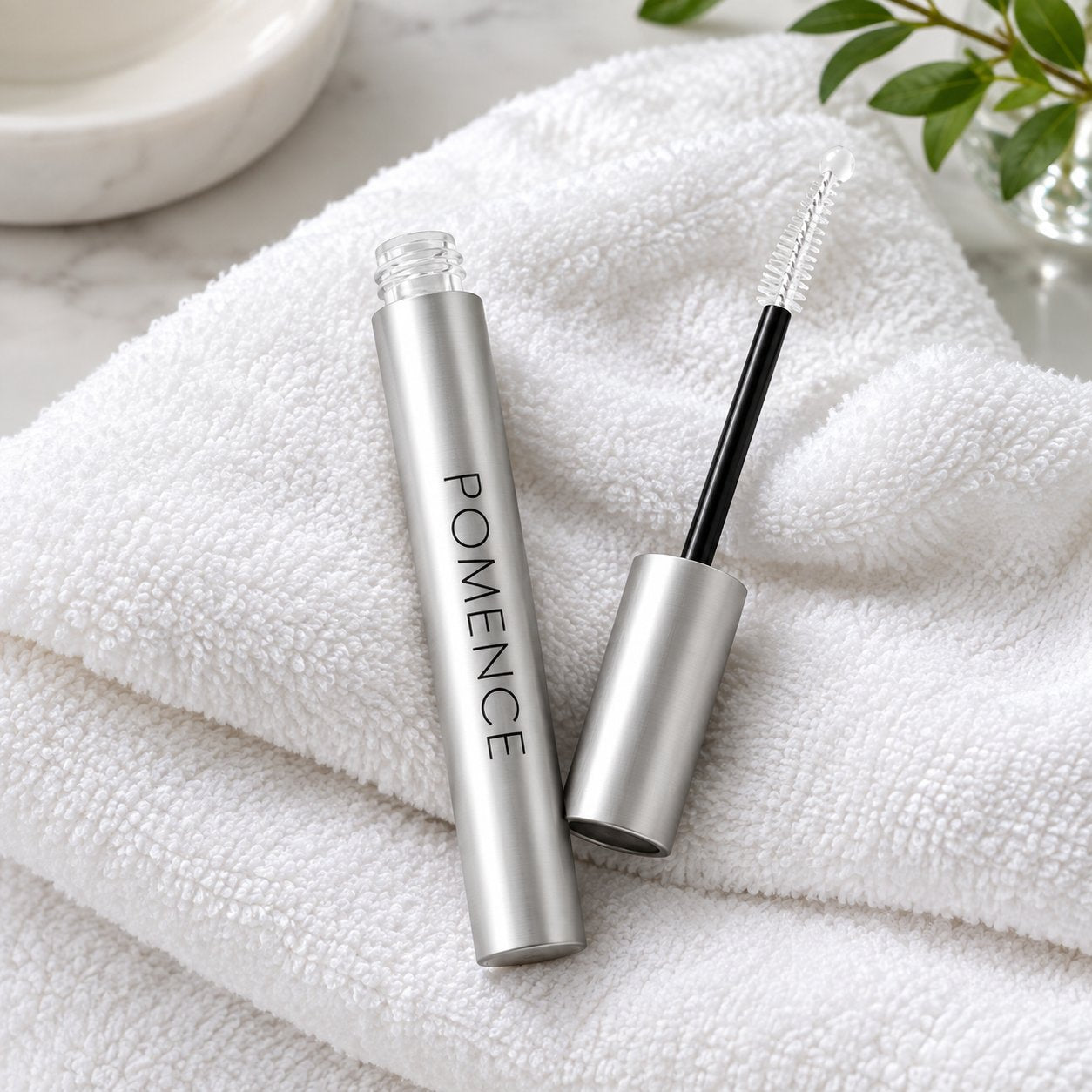 The Pomence Eyelash Growth Serum tube lying on a soft towel