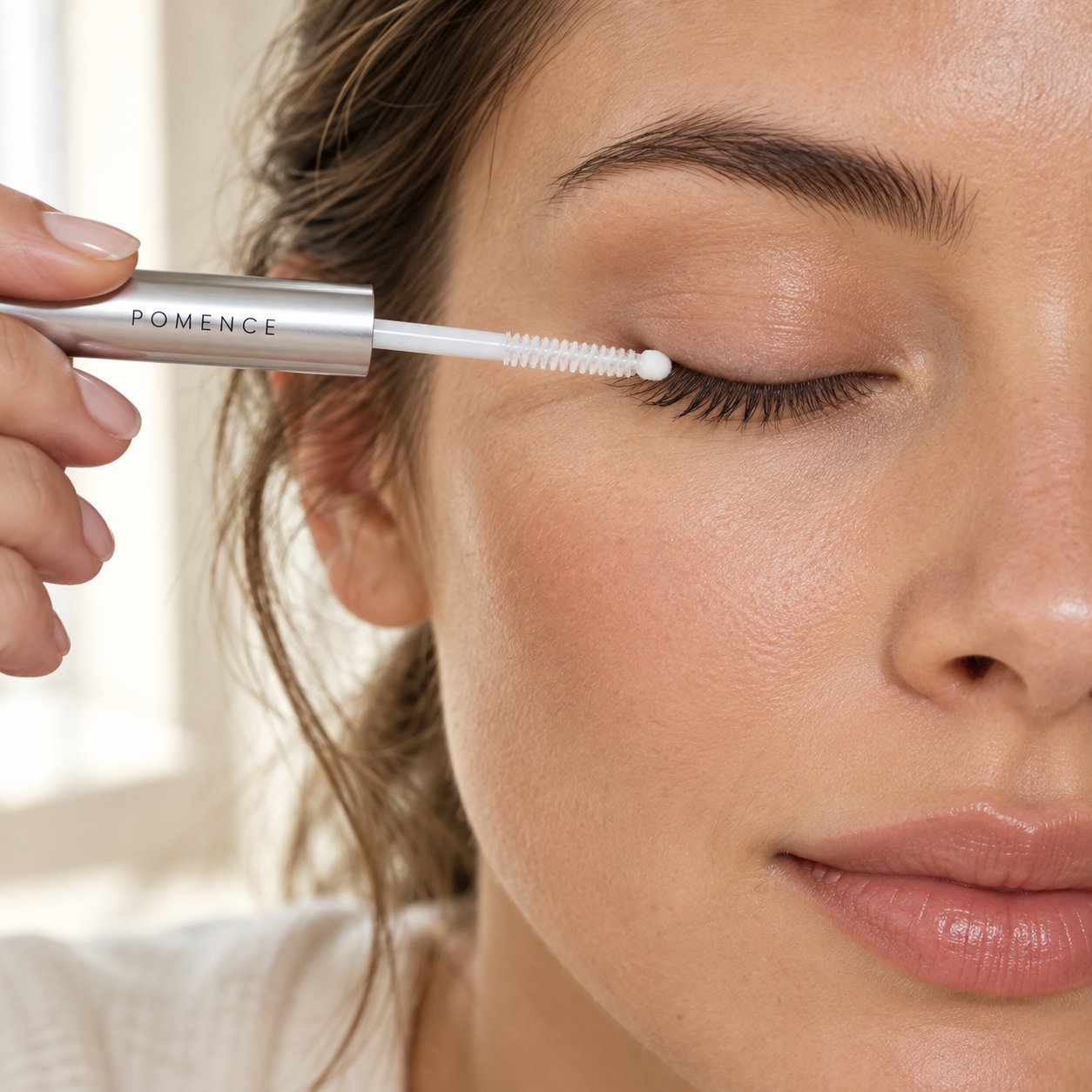 Close-up of a woman running the small ball tip of the Pomence serum wand along her upper lash line