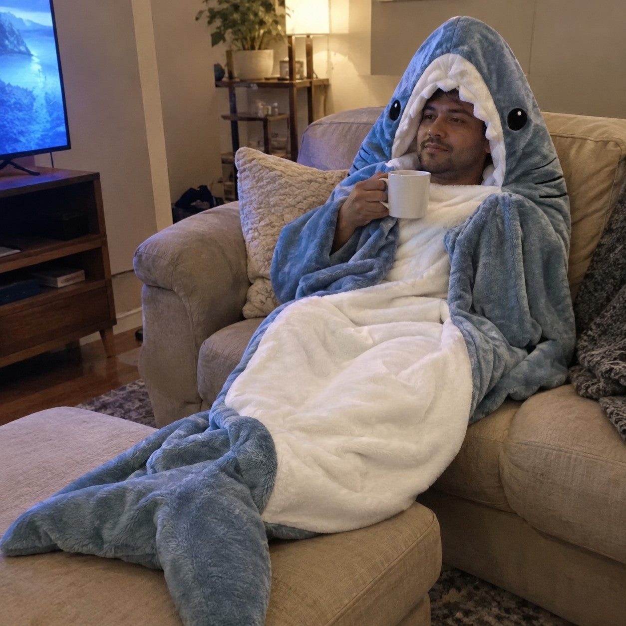 Man wrapped in a shark blanket on a sofa with a mug