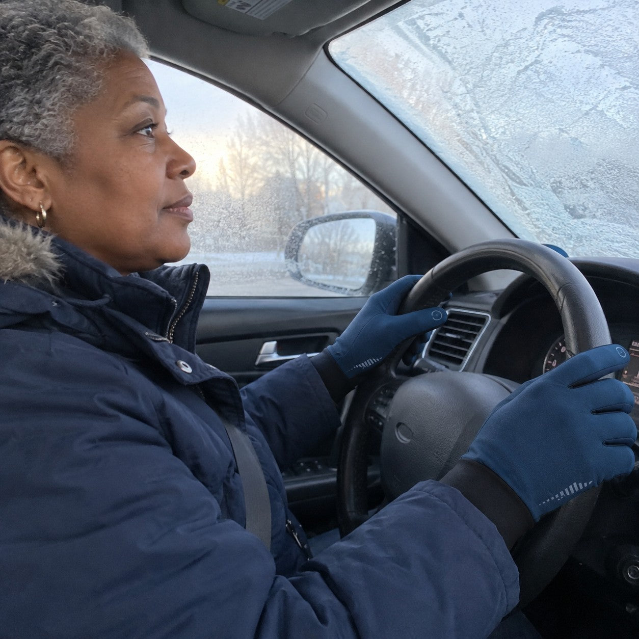 Gloved hands on a steering wheel by a frosted windshield